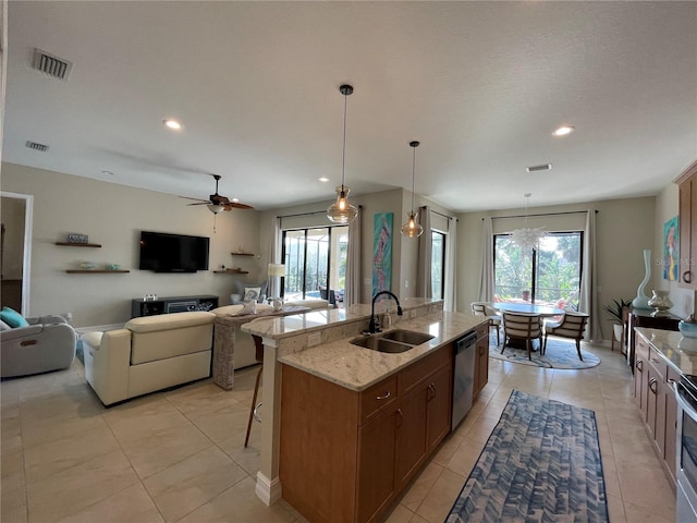 kitchen featuring sink, light stone counters, dishwasher, pendant lighting, and a kitchen island with sink