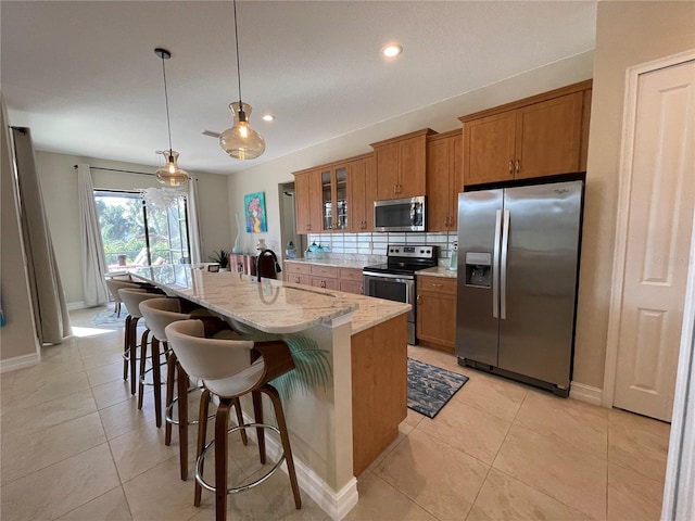 kitchen featuring stainless steel appliances, decorative backsplash, an island with sink, a kitchen bar, and decorative light fixtures