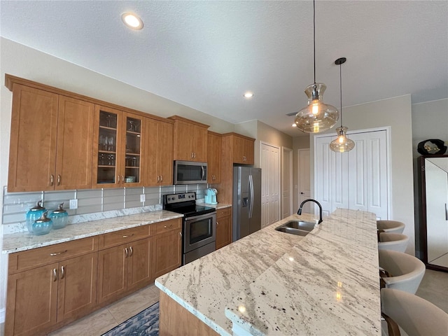 kitchen featuring sink, appliances with stainless steel finishes, hanging light fixtures, light stone counters, and a kitchen bar