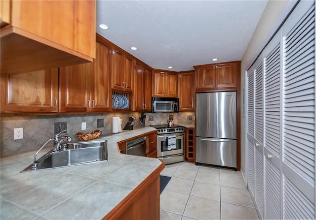 kitchen featuring appliances with stainless steel finishes, tasteful backsplash, sink, light tile patterned floors, and tile counters