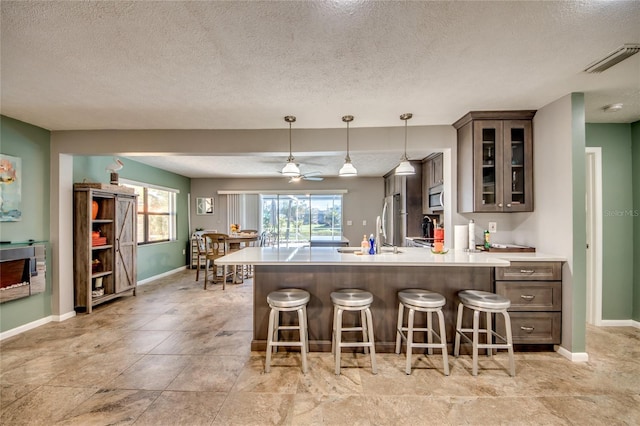 kitchen with ceiling fan, a textured ceiling, decorative light fixtures, dark brown cabinets, and stainless steel appliances