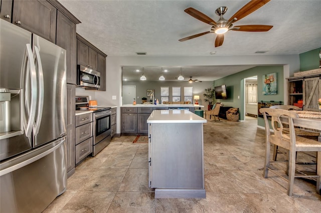 kitchen with appliances with stainless steel finishes, a textured ceiling, dark brown cabinetry, ceiling fan, and a center island