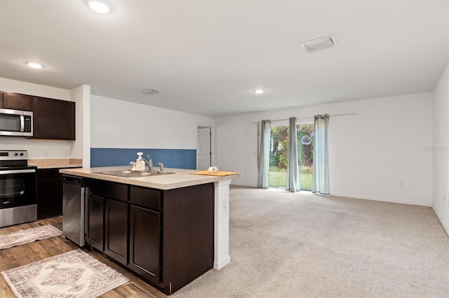 kitchen featuring dark brown cabinets, stainless steel appliances, sink, a kitchen island with sink, and light colored carpet