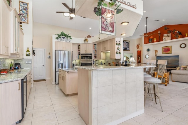 kitchen with stainless steel fridge, tasteful backsplash, light tile patterned floors, and an island with sink