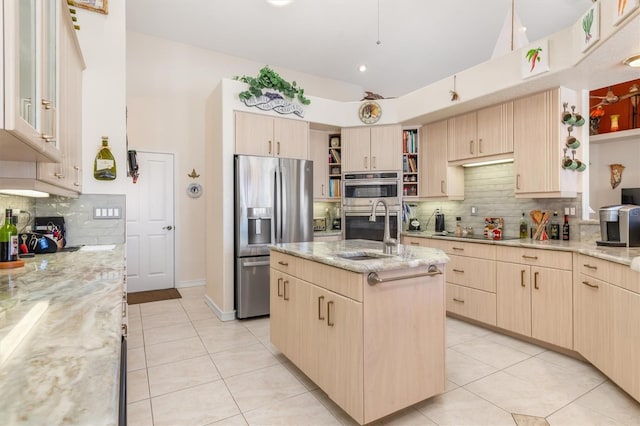 kitchen featuring light stone countertops, stainless steel appliances, sink, light brown cabinets, and an island with sink