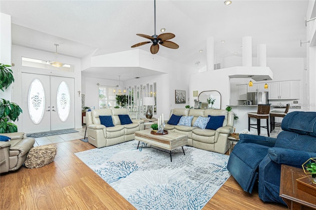 living room featuring ceiling fan with notable chandelier, light hardwood / wood-style floors, high vaulted ceiling, and french doors