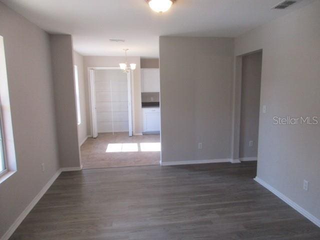 unfurnished room featuring dark wood-type flooring, plenty of natural light, and a notable chandelier