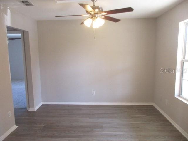 empty room with dark wood-style flooring, visible vents, ceiling fan, and baseboards