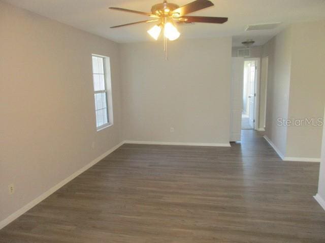 spare room with dark wood-style flooring, ceiling fan, and baseboards