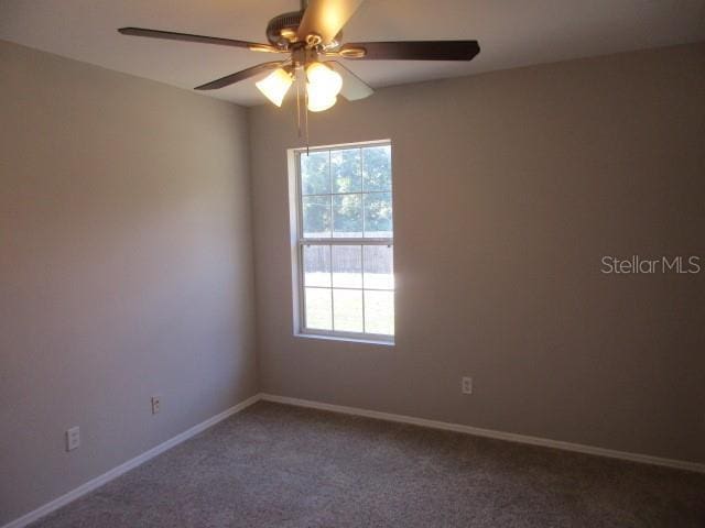 spare room with baseboards, ceiling fan, dark carpet, and a healthy amount of sunlight