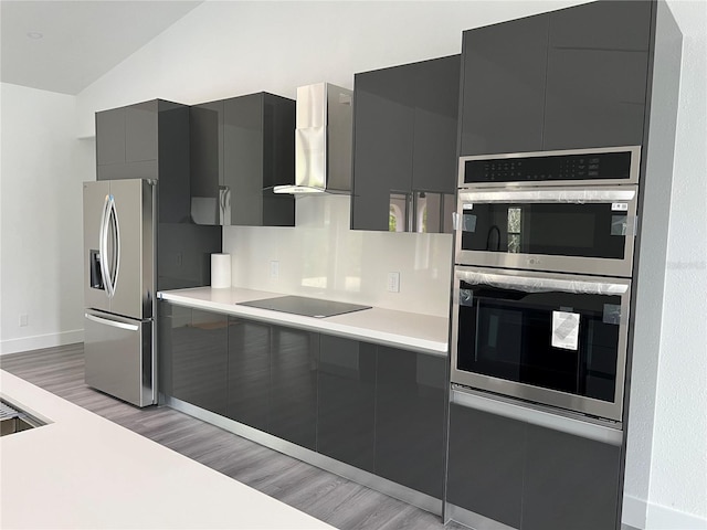 kitchen featuring wall chimney exhaust hood, stainless steel appliances, lofted ceiling, gray cabinets, and light wood-type flooring