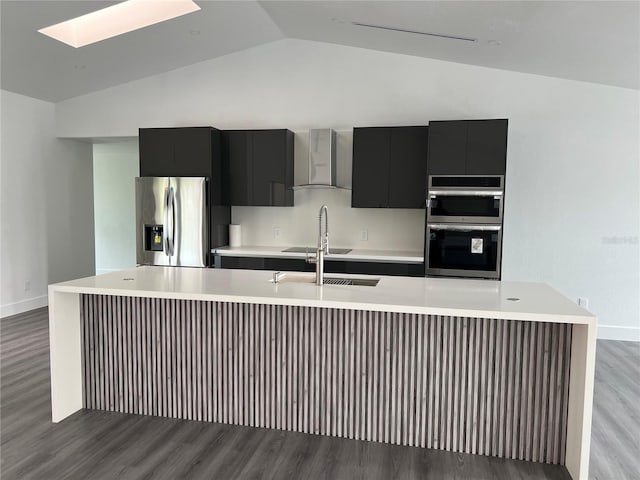 kitchen with stainless steel appliances, lofted ceiling with skylight, wall chimney range hood, a center island with sink, and light hardwood / wood-style floors