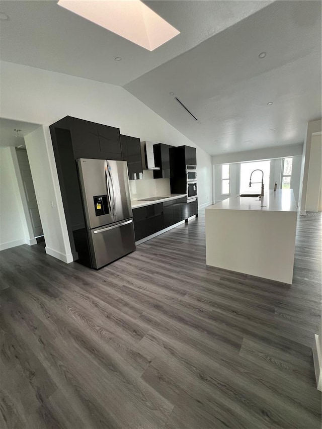 kitchen featuring sink, dark hardwood / wood-style floors, stainless steel refrigerator with ice dispenser, lofted ceiling with skylight, and an island with sink