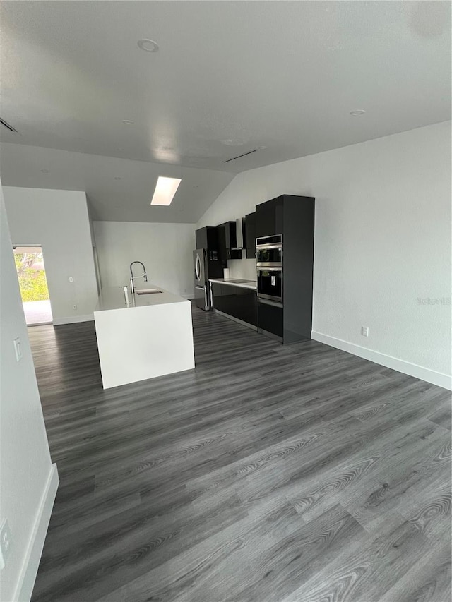 kitchen with lofted ceiling with skylight, sink, an island with sink, and dark wood-type flooring