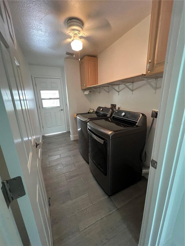 laundry room featuring cabinets, wood-type flooring, a textured ceiling, and washer and clothes dryer