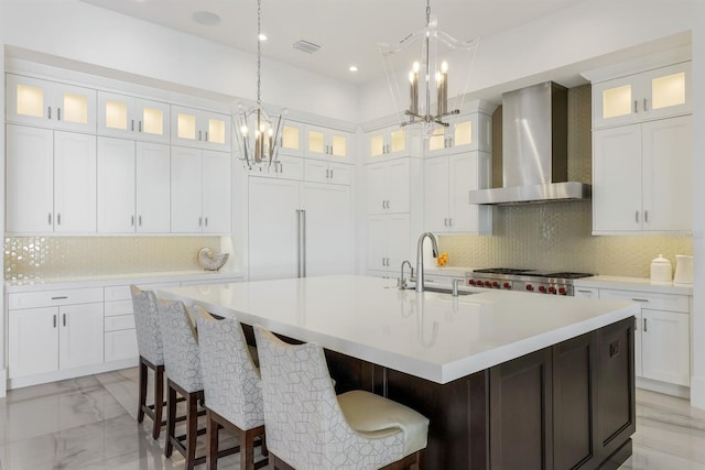 kitchen featuring white cabinets, sink, wall chimney range hood, and an island with sink