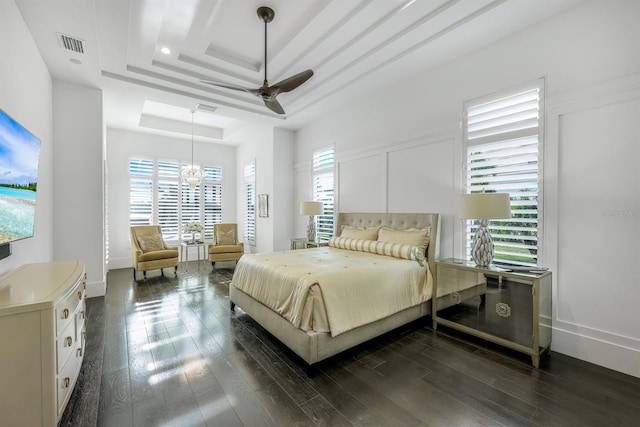 bedroom featuring ceiling fan with notable chandelier, dark hardwood / wood-style floors, and a raised ceiling