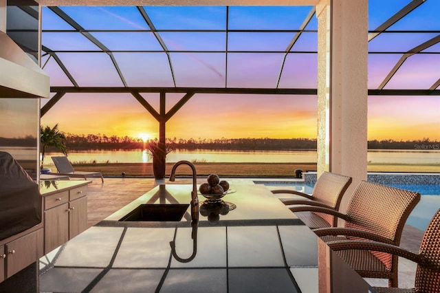 patio terrace at dusk featuring a water view, glass enclosure, and sink