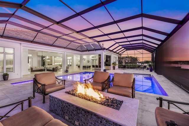 pool at dusk featuring glass enclosure, an outdoor living space with a fire pit, and a patio area