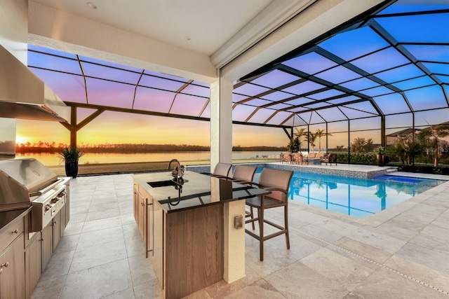 pool at dusk featuring a lanai, an outdoor wet bar, grilling area, area for grilling, and a water view