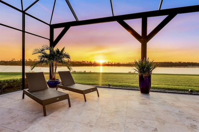 patio terrace at dusk with a water view, glass enclosure, and a lawn