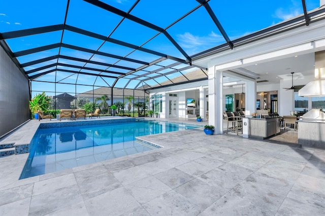 view of pool with glass enclosure, ceiling fan, a patio area, and exterior kitchen