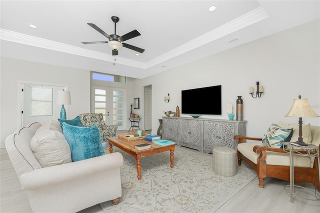 living room with ceiling fan, french doors, a raised ceiling, crown molding, and light wood-type flooring