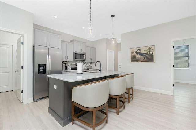 kitchen with gray cabinetry, sink, an island with sink, appliances with stainless steel finishes, and a breakfast bar area