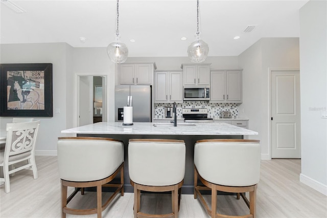 kitchen featuring appliances with stainless steel finishes, tasteful backsplash, pendant lighting, light hardwood / wood-style flooring, and an island with sink