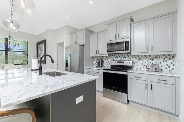 kitchen with light stone countertops, appliances with stainless steel finishes, backsplash, sink, and light hardwood / wood-style flooring