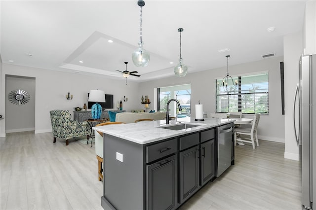 kitchen with appliances with stainless steel finishes, ceiling fan with notable chandelier, sink, light hardwood / wood-style floors, and an island with sink