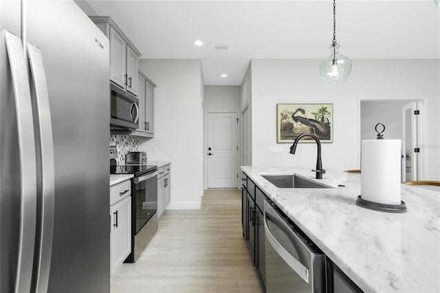 kitchen featuring sink, light stone counters, light hardwood / wood-style floors, pendant lighting, and appliances with stainless steel finishes