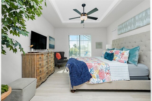 bedroom featuring access to outside, light hardwood / wood-style floors, ceiling fan, and a tray ceiling