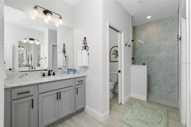 bathroom with hardwood / wood-style flooring, vanity, toilet, and a tile shower