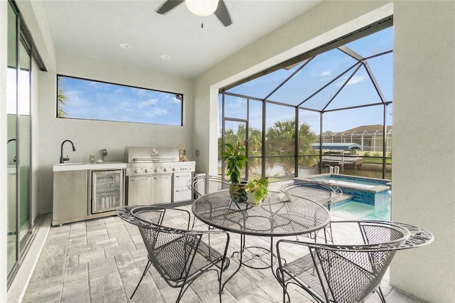 view of patio / terrace featuring glass enclosure, an outdoor kitchen, ceiling fan, an in ground hot tub, and area for grilling