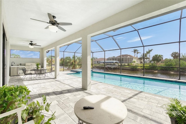 view of swimming pool with glass enclosure, a water view, ceiling fan, exterior kitchen, and a patio