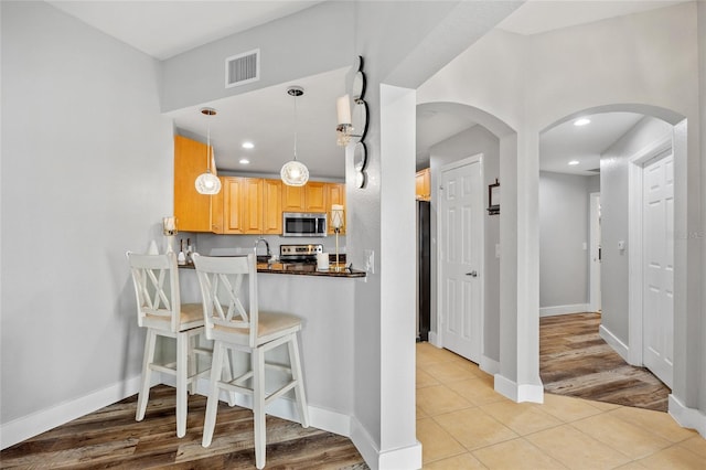 kitchen with a breakfast bar, pendant lighting, light tile patterned floors, and stainless steel appliances