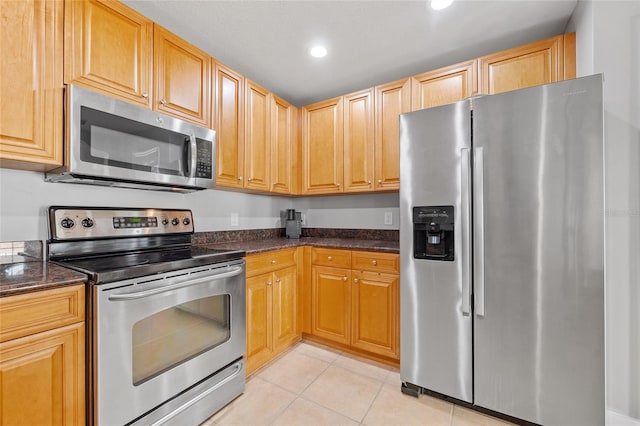 kitchen with light tile patterned floors, dark stone counters, and appliances with stainless steel finishes