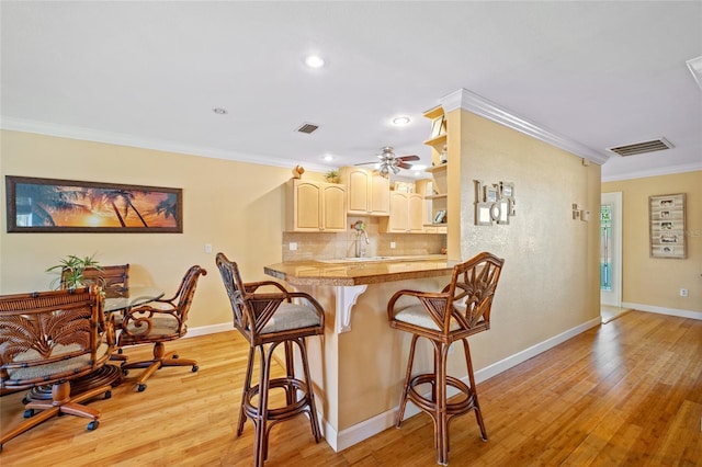 kitchen featuring light hardwood / wood-style flooring, decorative backsplash, ornamental molding, kitchen peninsula, and a breakfast bar area