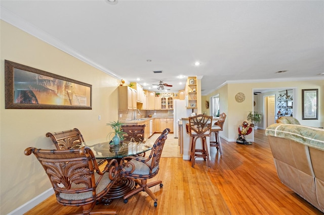 dining room with ceiling fan, light wood-type flooring, sink, and ornamental molding