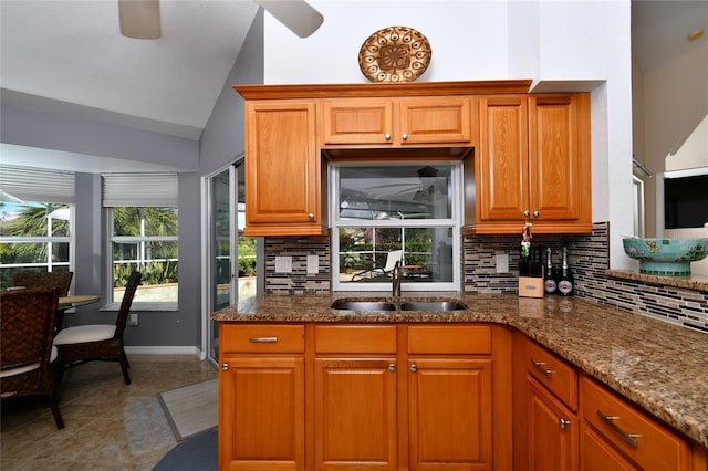 kitchen featuring tasteful backsplash, vaulted ceiling, dark stone counters, and sink