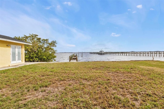 view of yard featuring a water view, a dock, and french doors