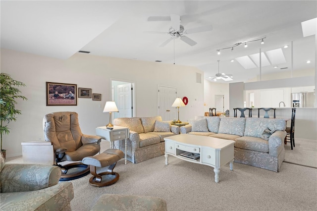 living room featuring rail lighting, light colored carpet, ceiling fan, and vaulted ceiling with skylight