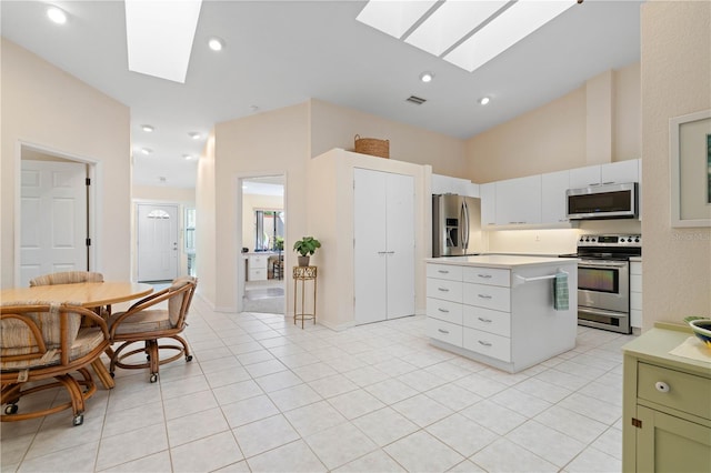 kitchen with a skylight, stainless steel appliances, green cabinetry, white cabinets, and light tile patterned flooring