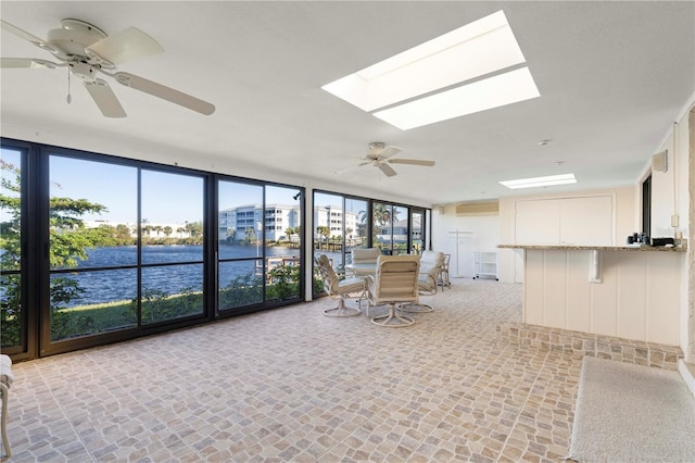 unfurnished sunroom featuring a skylight, ceiling fan, a water view, and a healthy amount of sunlight