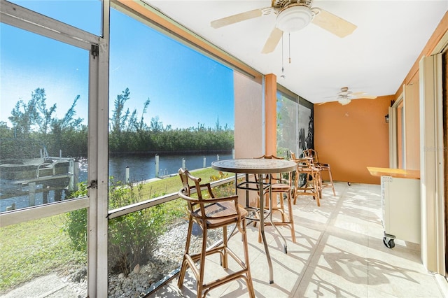 sunroom with ceiling fan and a water view