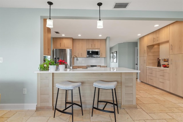 kitchen with light brown cabinetry, stainless steel appliances, decorative light fixtures, and sink