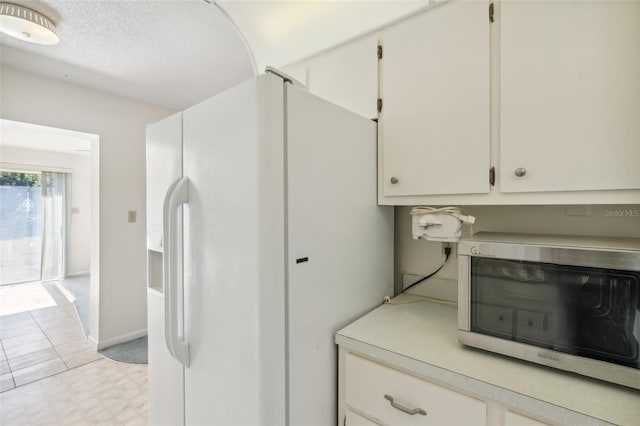 kitchen with white cabinetry, light tile patterned flooring, white fridge with ice dispenser, and a textured ceiling