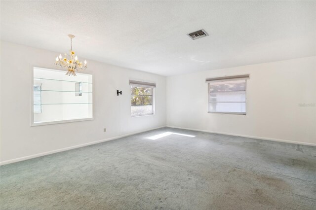 carpeted spare room with a textured ceiling and an inviting chandelier