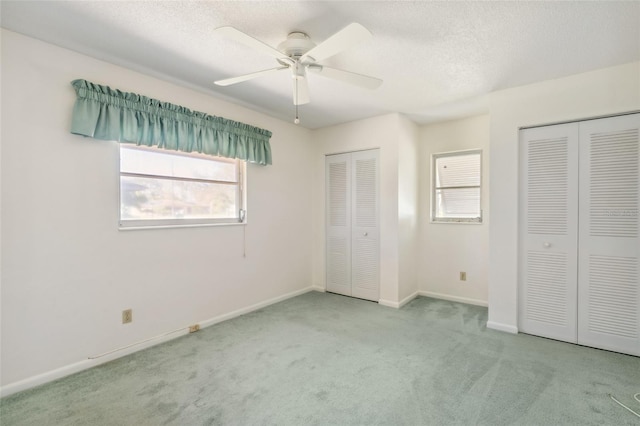 unfurnished bedroom with a textured ceiling, ceiling fan, light carpet, and multiple closets